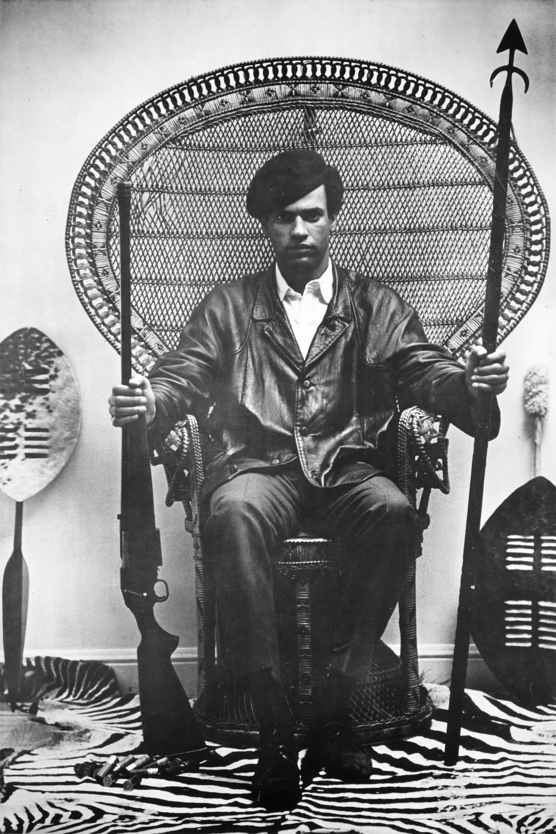 Huey P. Newton, cofondateur du Black Panther Party, assis dans le célèbre fauteuil en rotin, lance et fusil en main, vers 1968
