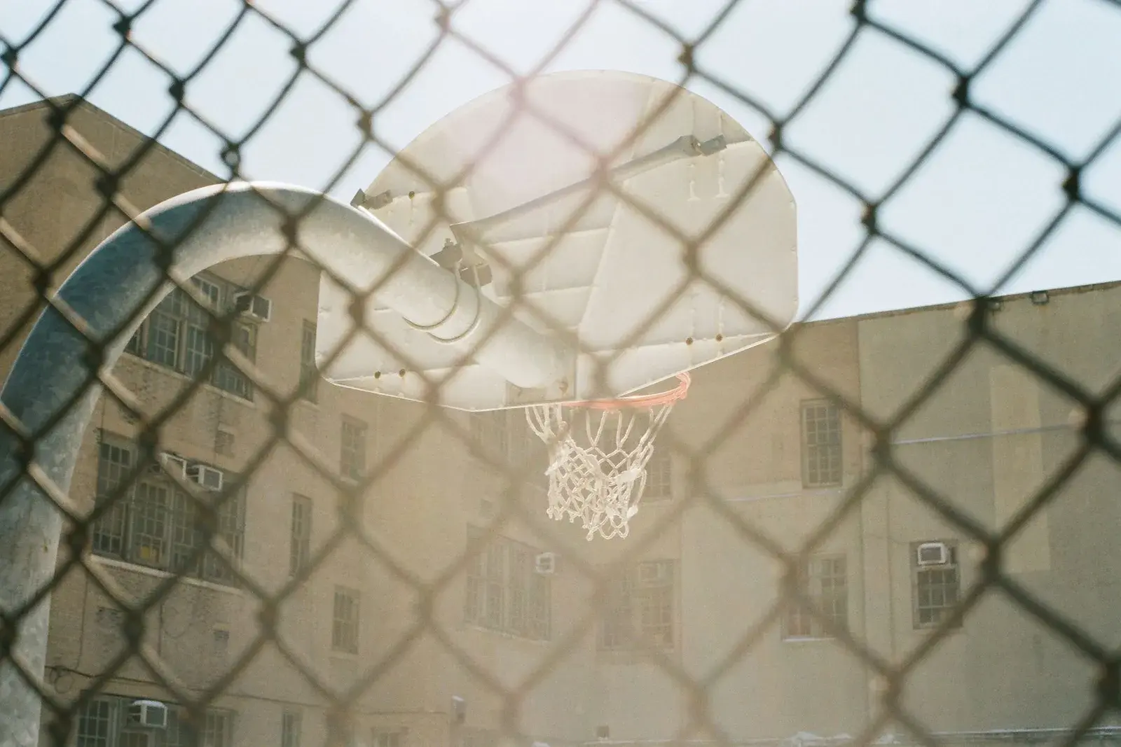 Panier de basket vu à travers un grillage, avec des immeubles en arrière-plan